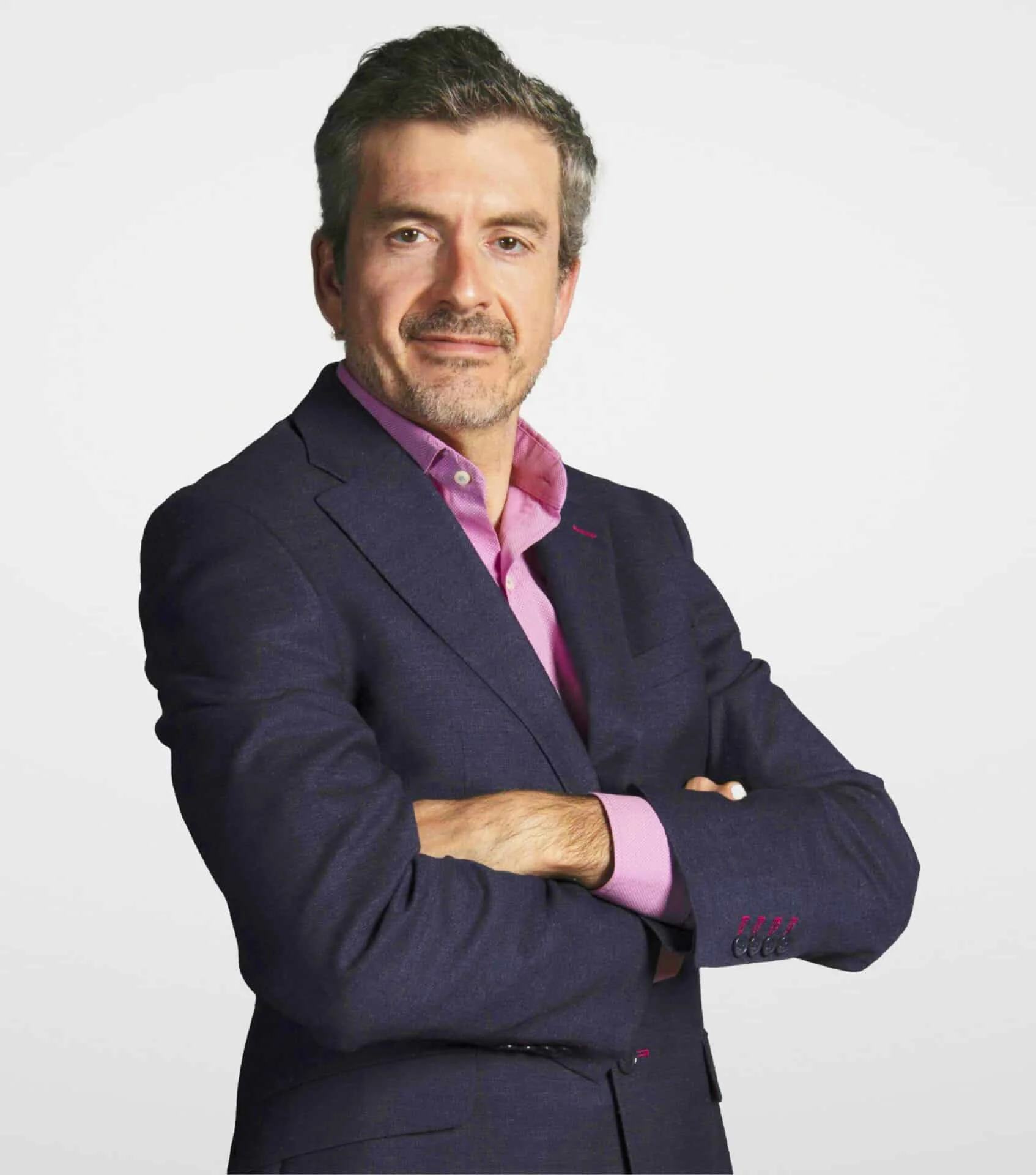 Retrato de medio cuerpo de Daniel Tovar Director de Acerta Latam, viste traje azul oscuro y camisa rosa, posando de brazos cruzados sobre un fondo blanco.