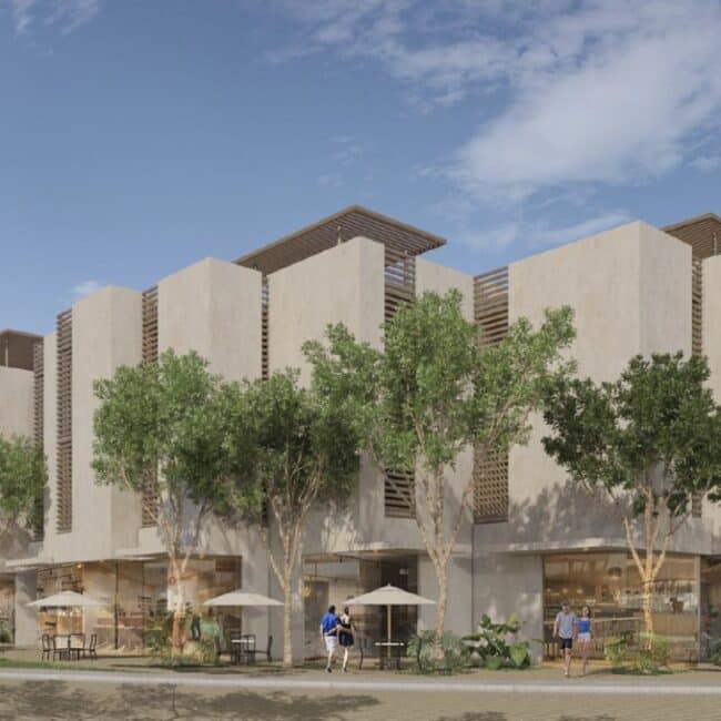 Área común de un hotel con terraza de madera, mesas exteriores, piscina rodeada de vegetación tropical y zona de bar bajo techado industrial.