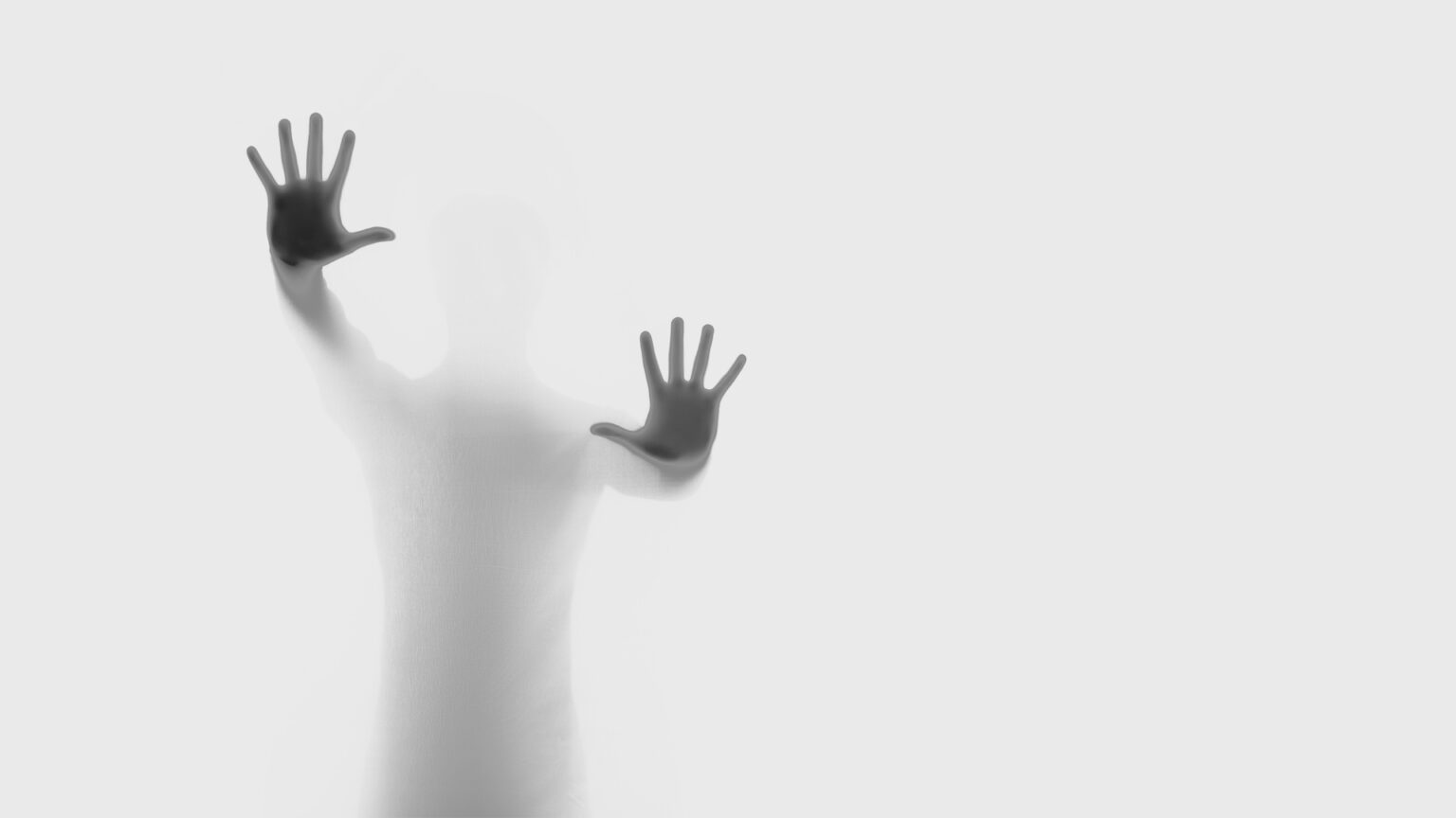 Silueta artística de una persona presionando sus manos contra una superficie blanca translúcida, creando un efecto de profundidad y transparencia.